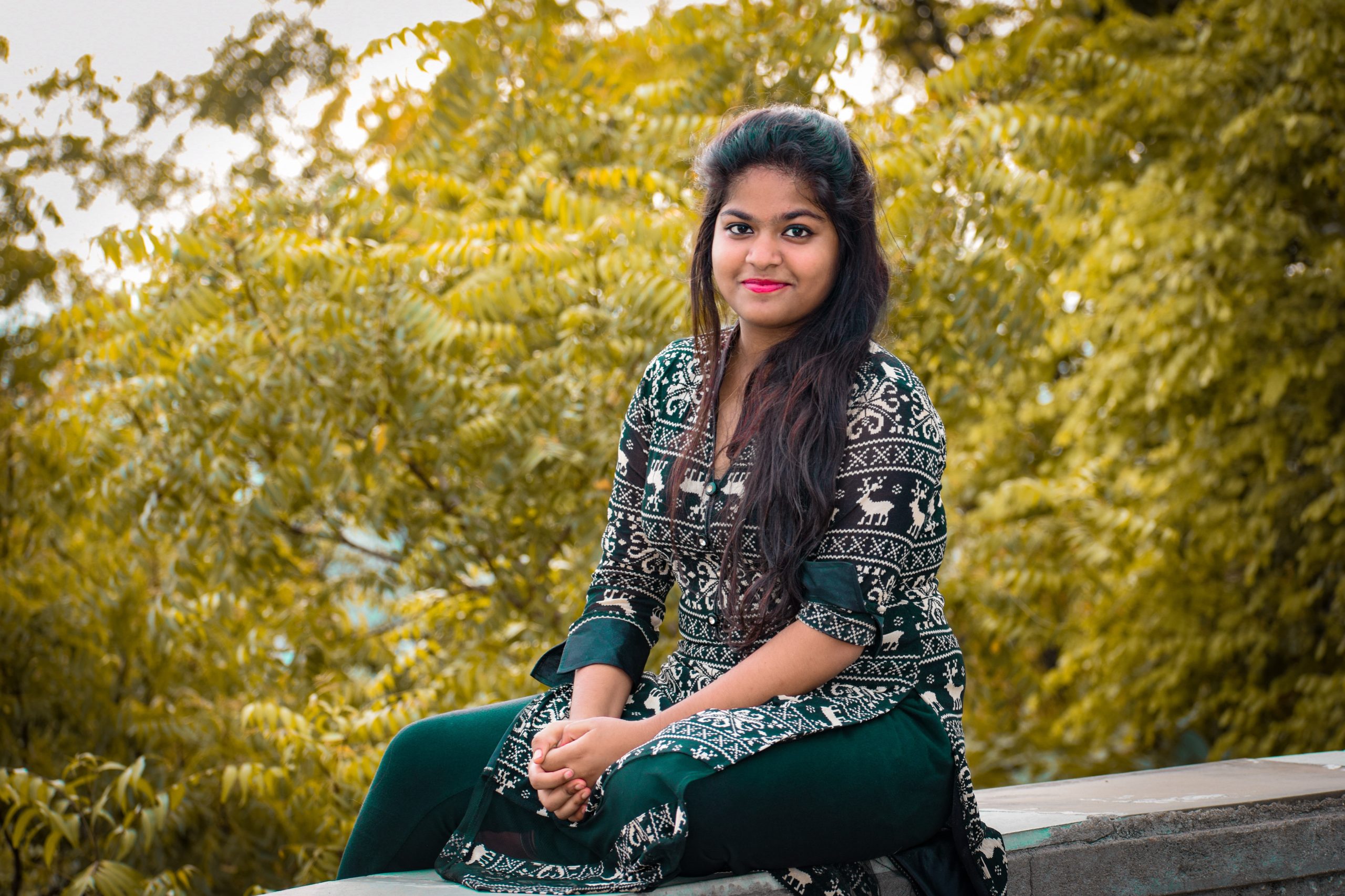 Young indian woman sitting on a wall and smiling at the camera